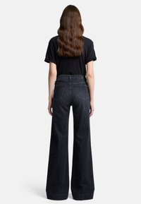 Jeans a vita alta e gamba larga in denim scuro con una rifinitura pulita, dotati di tasche posteriori e una vestibilità sagomata. Completati da una maglietta nera.