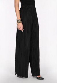 Black pleated wide-leg trousers with an elastic waistband, featuring vertical stripes for texture. Paired with studded black heels.