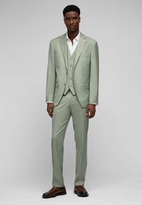 Hellgrüner maßgeschneiderter Anzug mit strukturiertem Finish, einreihige Jacke, Weste mit drei Knöpfen und braunen Dressschuhen.