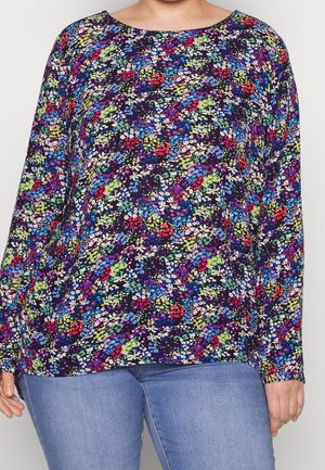 Langærmet top med et farverigt blomsterprint i blå, rød, grøn, lilla og hvid, båret med lyseblå jeans.