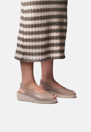 Füße in beigen Leder-Wedges mit Espadrilles und offenen Zehen, kombiniert mit einem braun-weiß gestreiften Strickrock.