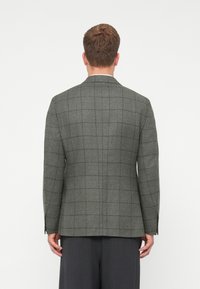 Pelēks šallēts žakets ar strukturētu dizainu, ar vienu šķēlumu, maigu faktūru un garām piedurknēm, savienots ar tumšiem biksēm.