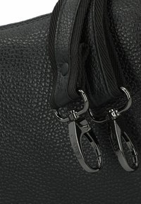 Bolso negro texturizado con un acabado en piedra, que cuenta con correas de nailon negro, ganchos metálicos y acentos de hardware suaves.