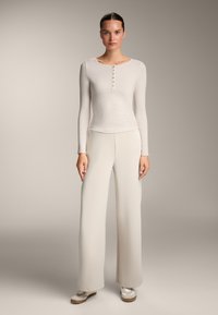 Hellbeige, geripptes Langarmoberteil mit rundem Halsausschnitt und fünf Knöpfen auf der Vorderseite, kombiniert mit leichten, weit geschnittenen Hosen in derselben Farbe.