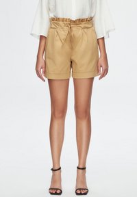 Khaki shorts with a drawstring waist, pleats at the front, and rolled hems; paired with black strappy sandals.