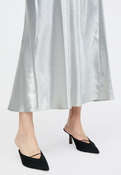 Črne mule z ostrim nosom in tankim petam, v kombinaciji z sijočo srebrno maxi krilo z mehkim, teksturiranim finišem in razširjenim krojem.
