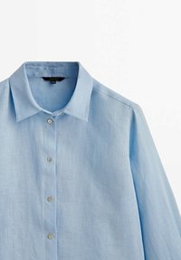 Camicia di lino azzurro chiaro con colletto classico, chiusura con bottoni e maniche lunghe. Presenta una texture sottile e dettagli con bottoni standard.