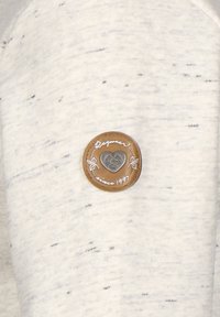 Tessuto grigio chiaro con una texture maculata presenta una toppa rotonda in pelle marrone, impresso con un cuore e "Dal 1997." Design semplice e informale.