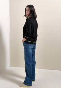 Svart långärmad topp med vit kant, i kombination med ljusblå, löst sittande jeans. Modellen står och vänder sig något bakåt.