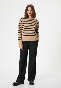 Maglione beige a righe con strisce orizzontali nere, scollo e orlo a coste, abbinato a pantaloni neri larghi e scarpe nere chunky.