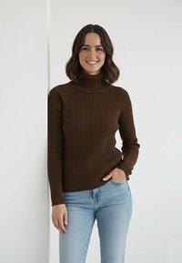 Brązowy prążkowany golf z długimi rękawami, zestawiony z jasnoniebieskimi dżinsami. Gładka tekstura i dopasowana sylwetka.