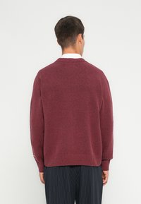 Suéter burdeos con cuello redondo, hombros caídos y puños acanalados. Tejido de punto texturizado con un corte relajado.