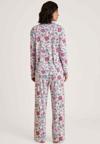 Floraal pyjama set met lange mouwen en wijd uitlopende broek. Witte basis met roze, blauwe en groene bloemenpatronen. Zacht materiaal, comfortabele pasvorm.