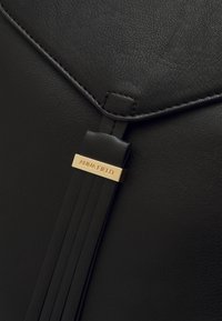 Bolso de cuero sintético negro con un acabado texturizado, con una placa dorada que dice "ANNA FIELD" y un detalle de correa plisada.
