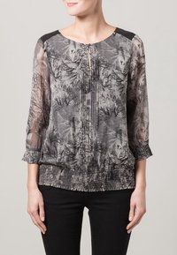 Przezroczysta bluzka z szaro-czarnym wzorem drzew, okrągłym dekoltem z otworem oraz elastycznym dołem i rękawami. Czarny akcent na ramionach.