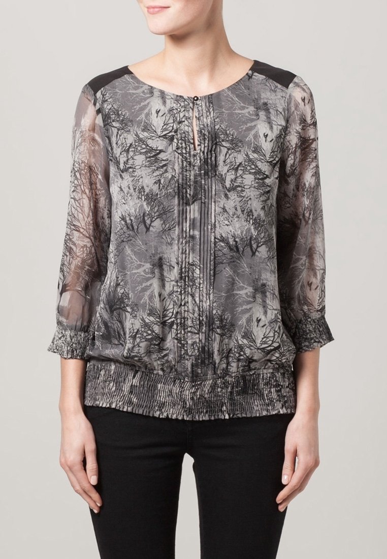 Przezroczysta bluzka z szaro-czarnym wzorem drzew, okrągłym dekoltem z otworem oraz elastycznym dołem i rękawami. Czarny akcent na ramionach.