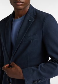 Marinblå blazer i slät tyg med skräddarsydd passform, med en ficka på bröstet och en subtil snusdosa i form av ett djur på laget.
