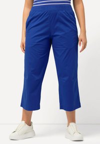 Blå cropped byxor med elastisk midja, sidofickor, slät tyg och avslappnad passform, som är ihop med vita sneakers.