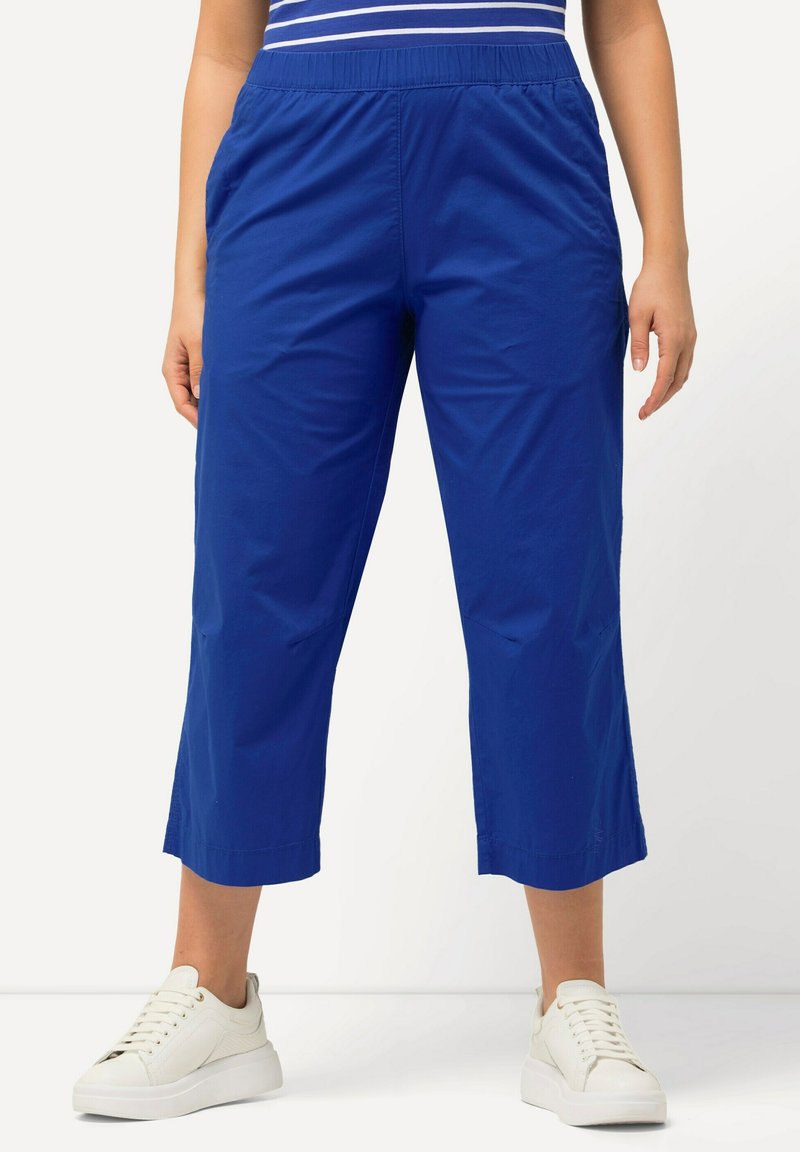 Blå cropped byxor med elastisk midja, sidofickor, slät tyg och avslappnad passform, som är ihop med vita sneakers.