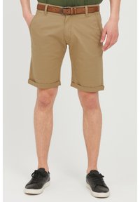Khaki szorty z podwiniętymi mankietami, wykonane z lekkiego materiału. Z paskiem w kolorze brązowym ze skóry. Połączone z czarnymi sneakersami.