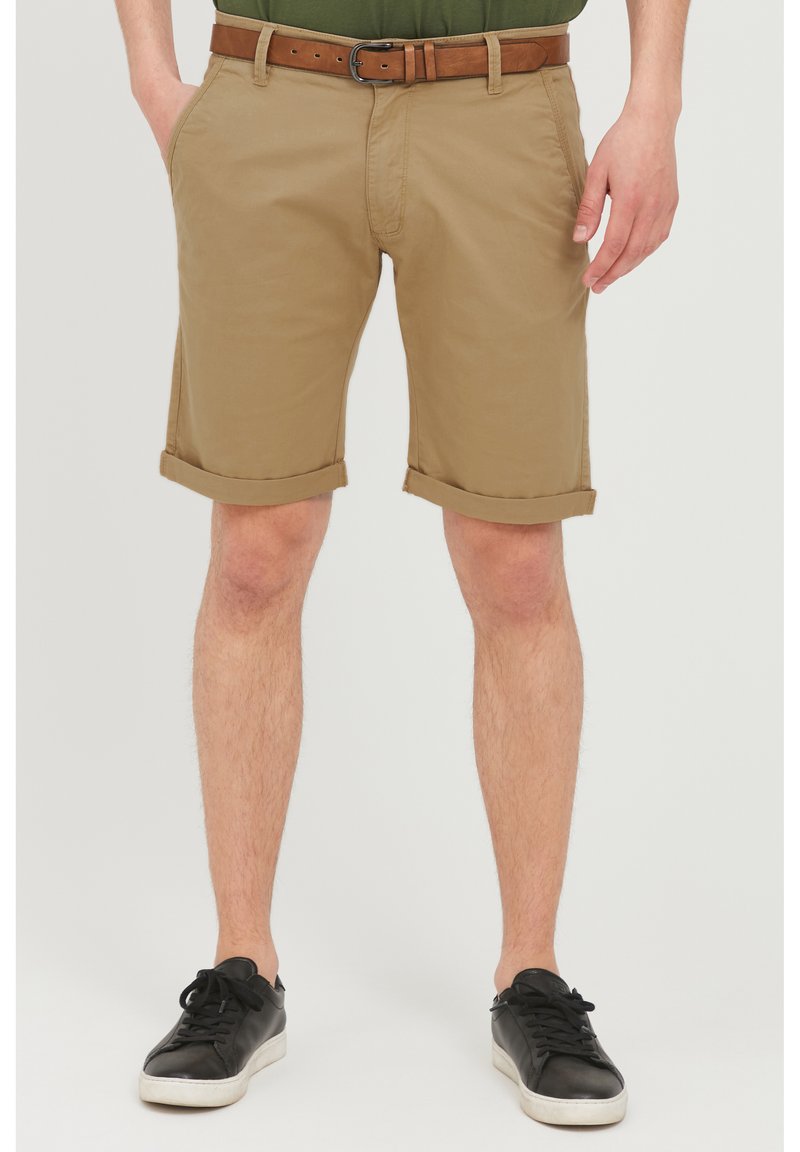 Khaki szorty z podwiniętymi mankietami, wykonane z lekkiego materiału. Z paskiem w kolorze brązowym ze skóry. Połączone z czarnymi sneakersami.