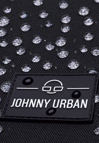 Vízálló fekete szövet vízcseppekkel; jellemzője egy téglalap alakú logófoglalat, amelyen fehér betűkkel az "JOHNNY URBAN" felirat található.