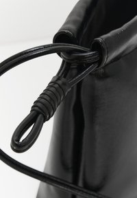 Borsa a secchiello in pelle nera con una finitura liscia, chiusura a coulisse e manico testurizzato. Presenta un design pulito e minimale.