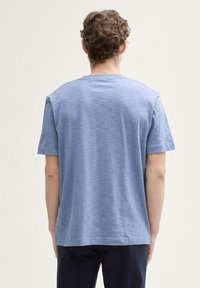 Camiseta corta de manga azul hecha de tejido ligero, con cuello redondo y un ajuste holgado, con una superficie suave y ligeramente texturizada.