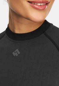 Czarny top sportowy z okrągłym dekoltem, wykonany z teksturowanej tkaniny, z kontrastowymi szwami i delikatnym logo z przodu.