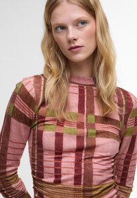 Langärmeliges Oberteil aus strukturiertem Strick, mit einem karierten Muster in Rosa, Braun und Grün, Raffung an den Seiten und hohem Kragen.
