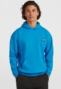 Sweatshirt bleu vif avec une capuche, une poche avant et des poignets côtelés. Présente un petit logo triangulaire sur la poitrine gauche. Texture de tissu douce.