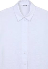 Camicia bianca a maniche corte realizzata in tessuto testurizzato, con colletto e una fila di bottoni sul davanti. L'etichetta riporta "Terranova" con la tag di dimensione "S".