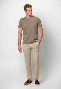 Brązowa koszulka z krótkim rękawem, beżowe dopasowane spodnie i ciemne buty wsuwane. Gładki materiał, dopasowany krój i neutralna paleta kolorów.