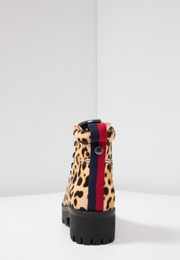 Bottines à imprimé léopard avec un tissu texturé, semelle en caoutchouc noir, et un accent rayé rouge et bleu à l'arrière.