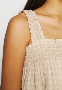 Top tank beige arricciato con spalline volantee e un design a quadri testurizzato. Materiale in cotone morbido con vestibilità comoda.