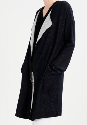 Long cardigan noir marine avec une capuche et un col gris clair. Il dispose de deux poches à l'avant et d'une coupe décontractée et oversized. Tissu doux et texturé.