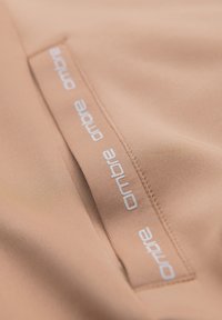 Tissu beige avec une bande cousue affichant le texte blanc répété « ombre » le long de la couture.
