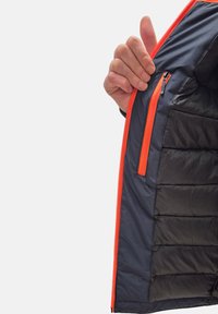 Interno di una giacca puffer blu navy con accenti arancioni sulla cerniera. Presenta imbottitura trapuntata e una piccola tasca con cerniera. Texture liscia in tutto.