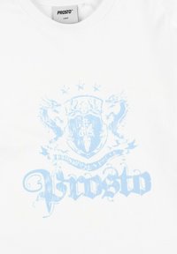 Biała bawełniana koszulka z jasnoniebieskim wzorem graficznym, obejmującym tarczę i smoki, z napisem "Prosto" w stylizowanej czcionce.