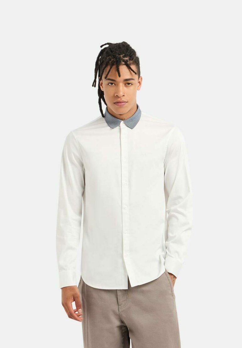 Camicia bianca a maniche lunghe con colletto a camicia grigio a contrasto, realizzata in tessuto liscio. Bottoni lungo la parte anteriore e polsini su misura.