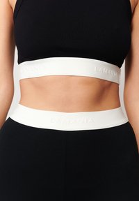 Čierny crop top s bielym elastickým pásom s nápisom "LAMANIA." Tkanina je hladká, priliehavá a elastická, aby pohodlne obopínala telo.