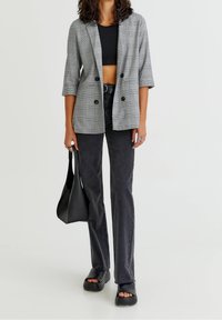 Blazer à carreaux gris à manches courtes, associé à un haut noir ajusté et un jean. Des sandales noires à bout ouvert et un sac à main noir complètent le look.
