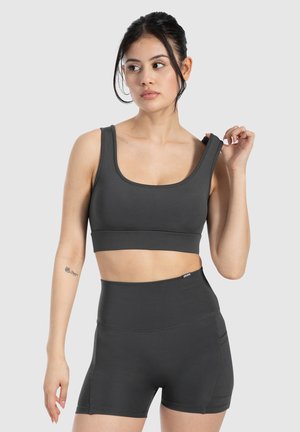 Dunkelgrauer Sport-BH mit quadratischem Ausschnitt und breiten Trägern, kombiniert mit hochgeschnittenen Shorts, die über Seitennahttaschen und ein elegantes Design verfügen.