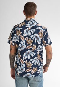 Camicia a maniche corte in tessuto blu scuro con ampi motivi floreali bianchi e marroni. Collo a scollatura, vestibilità rilassata e orlo dritto.