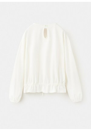 Vit långärmad blus med resår i fållen, nyckelhål bak med en knapp, visad mot en enfärgad bakgrund.