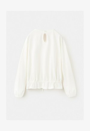 Blouse blanche à manches longues avec ourlet élastiqué, fermeture au dos en forme de goutte d'eau sécurisée par un seul bouton, présentée sur un fond uni.