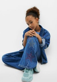 Denimjacka och byxor med stjärndekorationer i röd och silver, matchade med ljusblå sneakers. Texturen är mjuk och passformen är avslappnad.