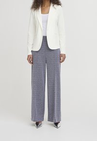 Blazer bianco con apertura frontale, abbinato a pantaloni grigi a vita alta e gamba larga con motivo a spina di pesce. Tacchi argento appuntiti completano il look.