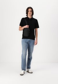 Svart kortermet polo-skjorte med glidelås, blå denim jeans og hvite sneakers. Personen bærer en liten svart crossover-veske.
