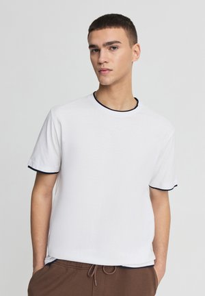 Maglietta bianca in cotone con maniche corte, collo e bordi delle maniche blu navy. Tessuto piatto, vestibilità comoda e design semplice.